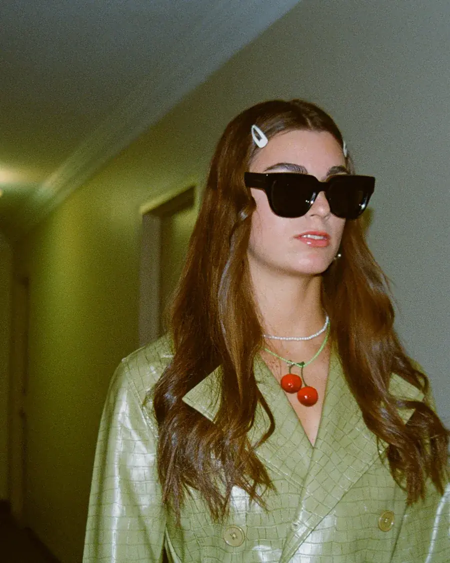 Retrato con gafas oscuras y chaqueta verde croco en un pasillo de hotel
